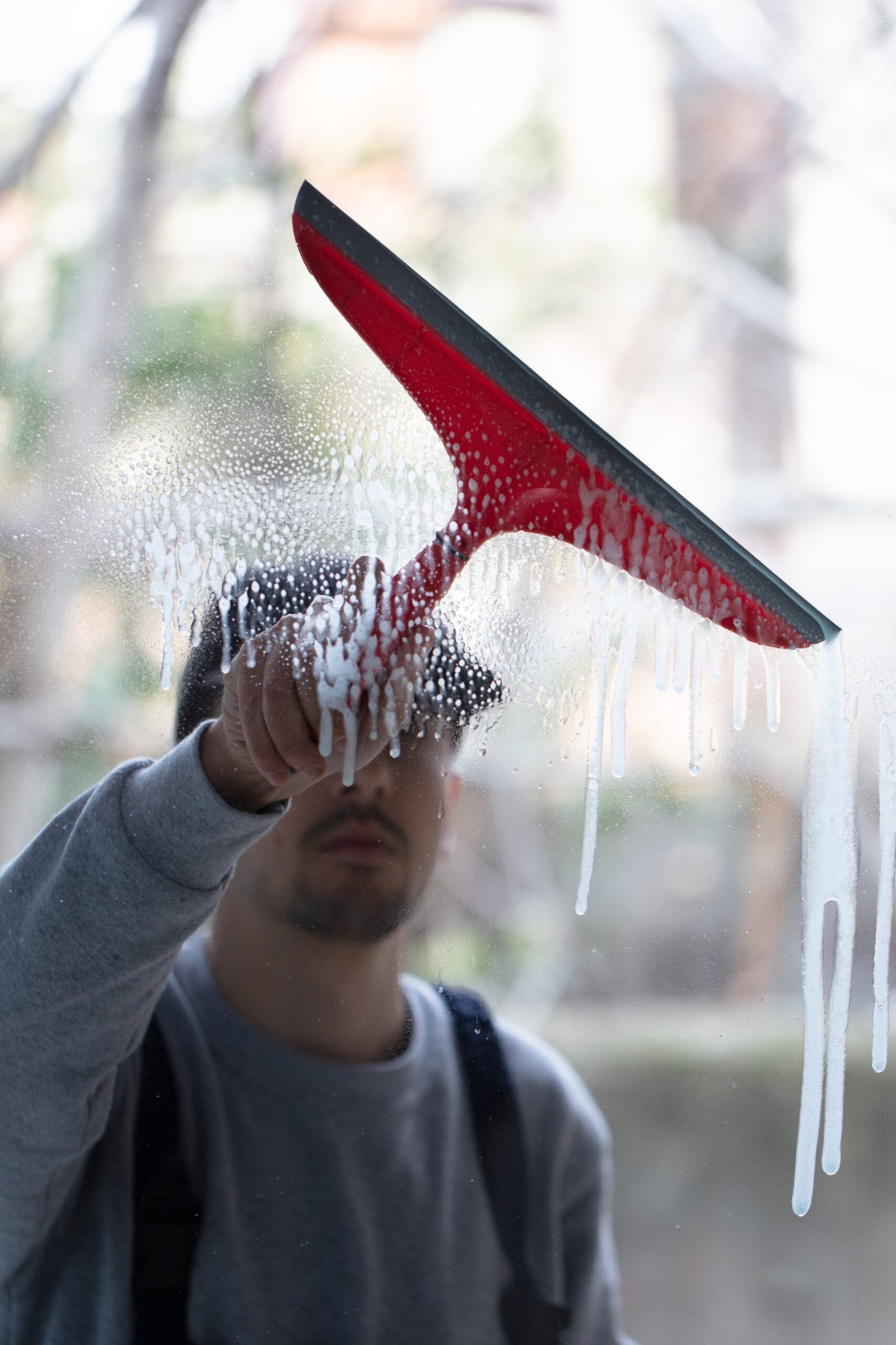 Closeup of a person cleaning windows with a red squeegee under the lights with a blurry background