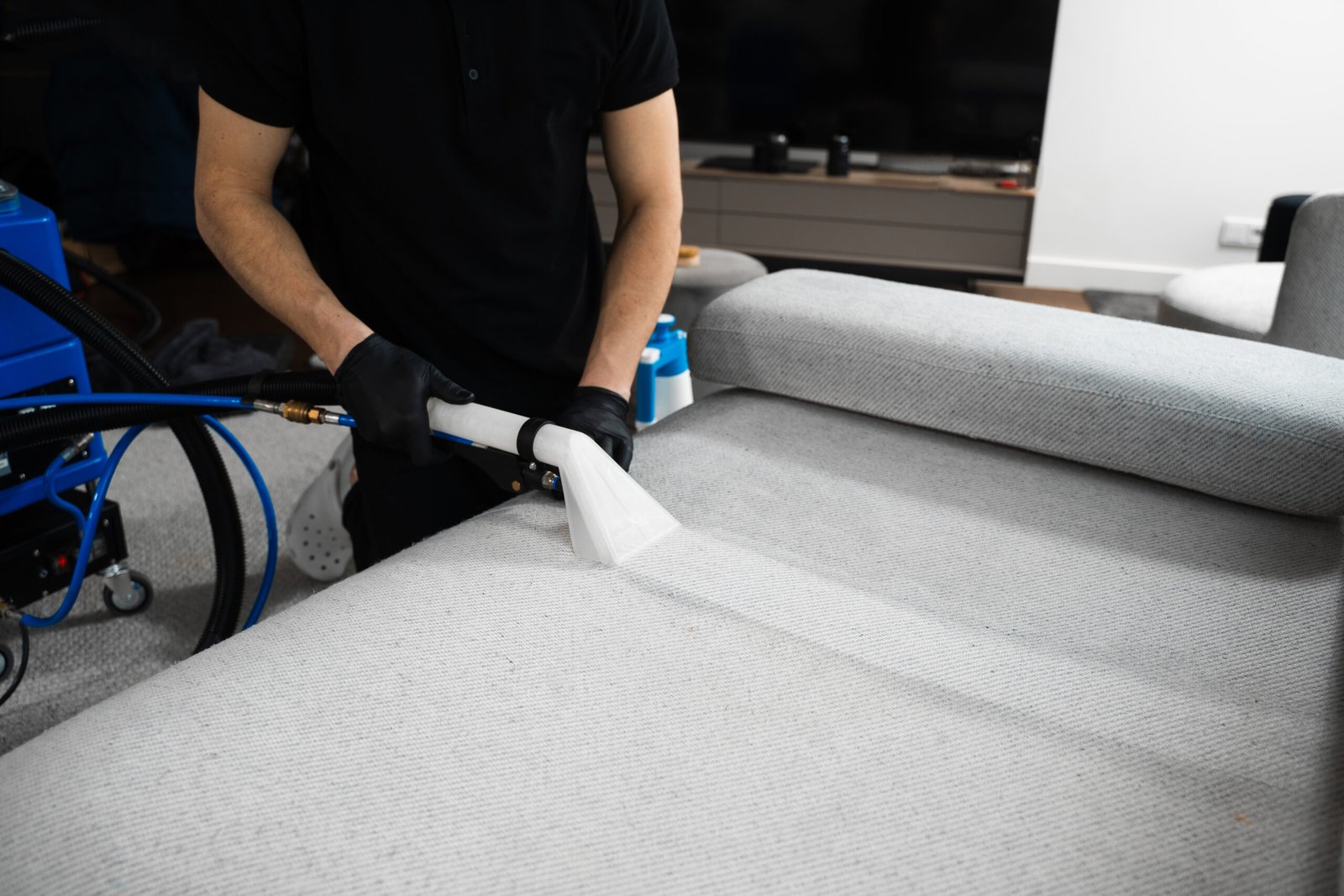 Cleaner is dry-cleaning sofa using extractor machine with detergent. Using extractor to refresh and clean from dust and stains upholstered furniture.