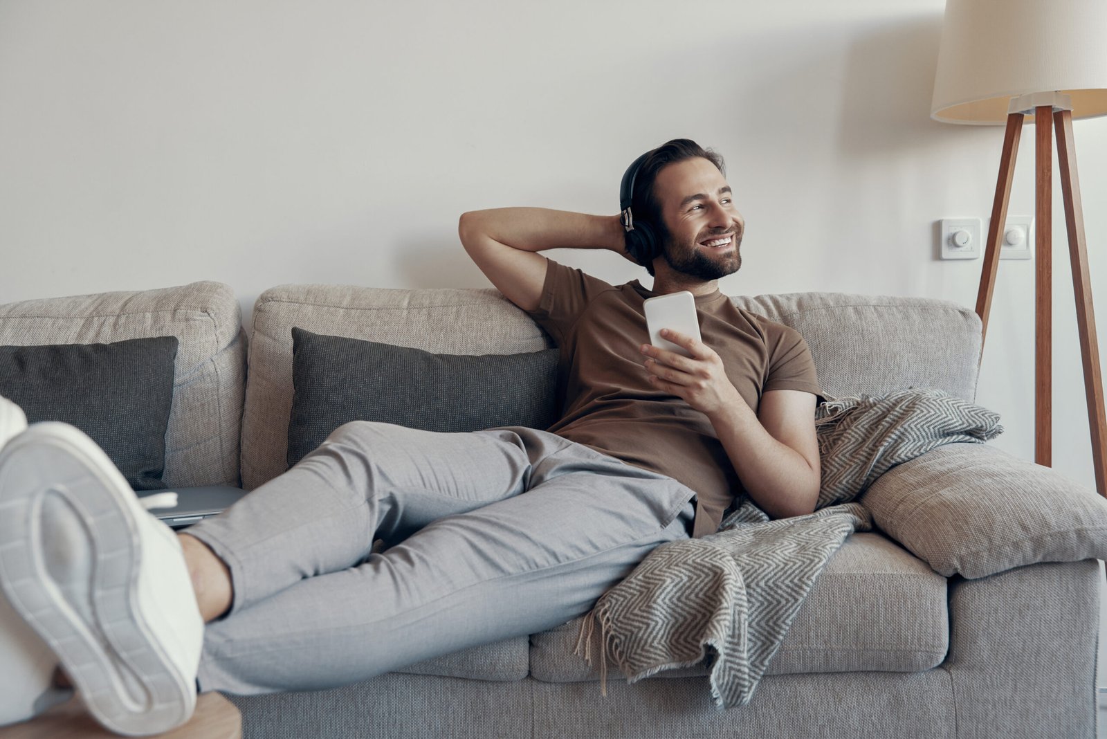 Carefree young man in headphones holding smart phone while relaxing on the couch at home